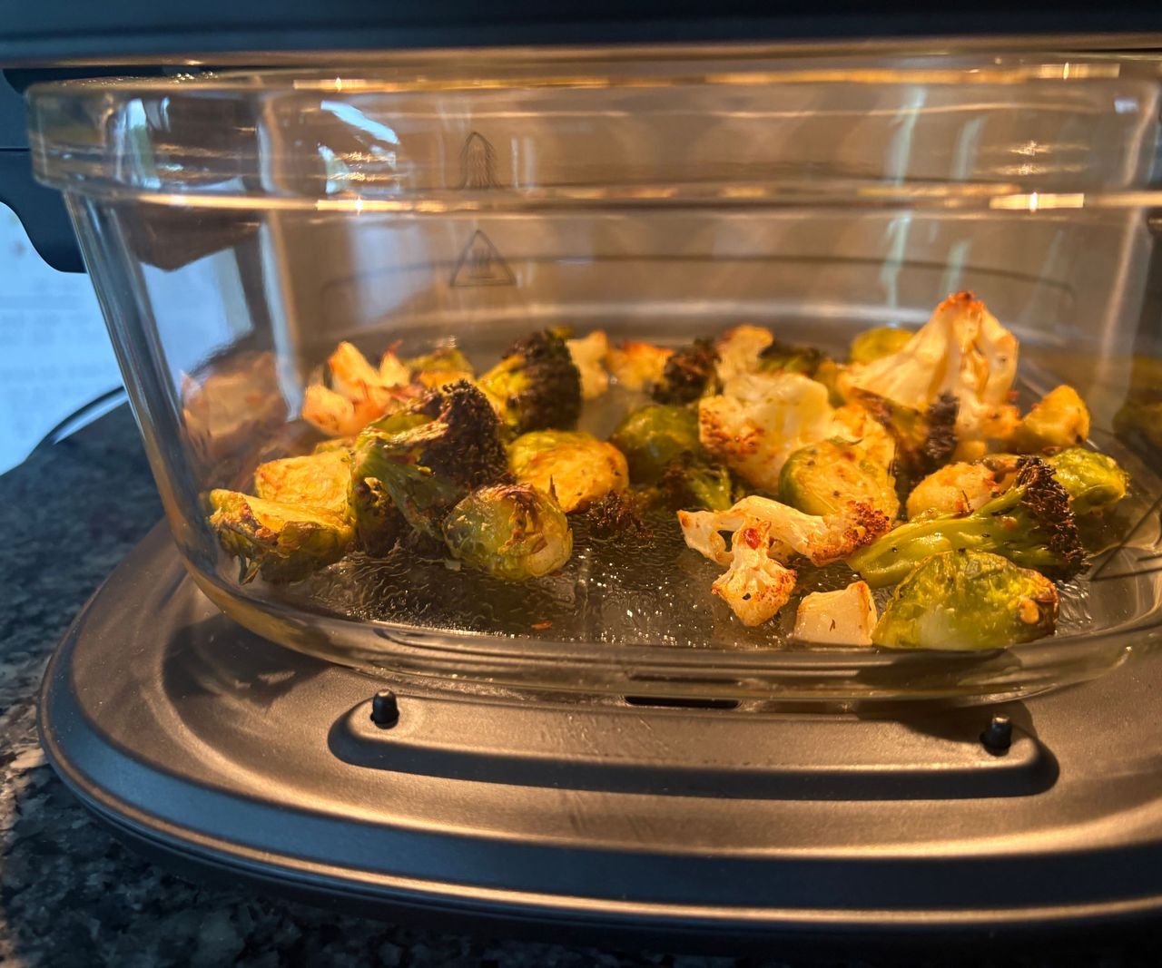 The Cuisinart glass air fryer on a granite countertop viewed from the side with roasted vegetables inside.