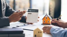 Hand pointing to calculator next to models of houses