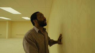 Chiwetel Ejiofor in Backrooms, where he's in an empty yellow room. He is touching a wall and looks scared.
