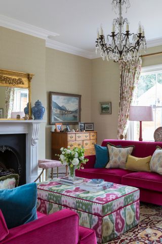 classic living room with matching pink velvet couches, fire place, vintage pieces, patterned ottoman, patterned drapes, lighting