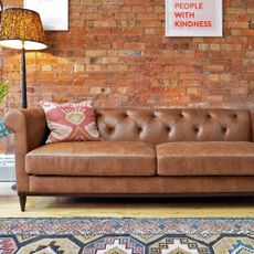 Swyft Chesterfield sofa in leather, in a living room with a lamp, rug, and a brown wall behind