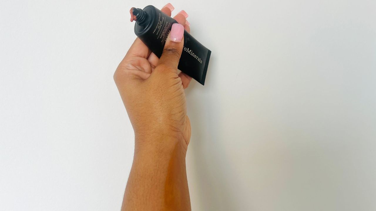 A person holding a black tinted moisturizer with SPF squeeze tube.