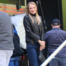 Uma Thurman wears dark wash jeans with a leather jacket and white Onitsuka Tiger Trainers