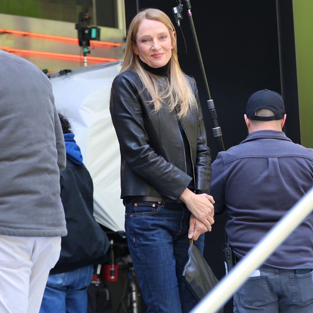 Uma Thurman wears dark wash jeans with a leather jacket and white Onitsuka Tiger Trainers