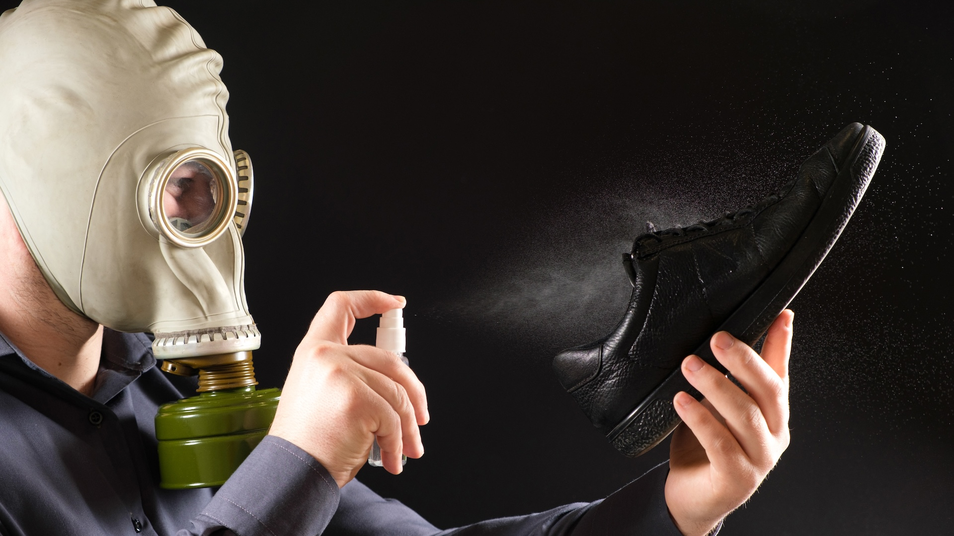 A man spraying a shoe wearing a gas mask 