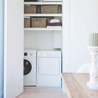 White utility room cuboard with washing machine and tumble dryer, with shelves above it