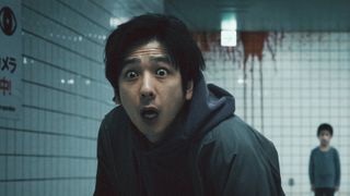 A shocked man standing in front of a bloody wall and a young boy.