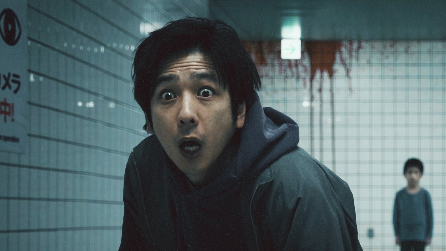 A shocked man standing in front of a bloody wall and a young boy.