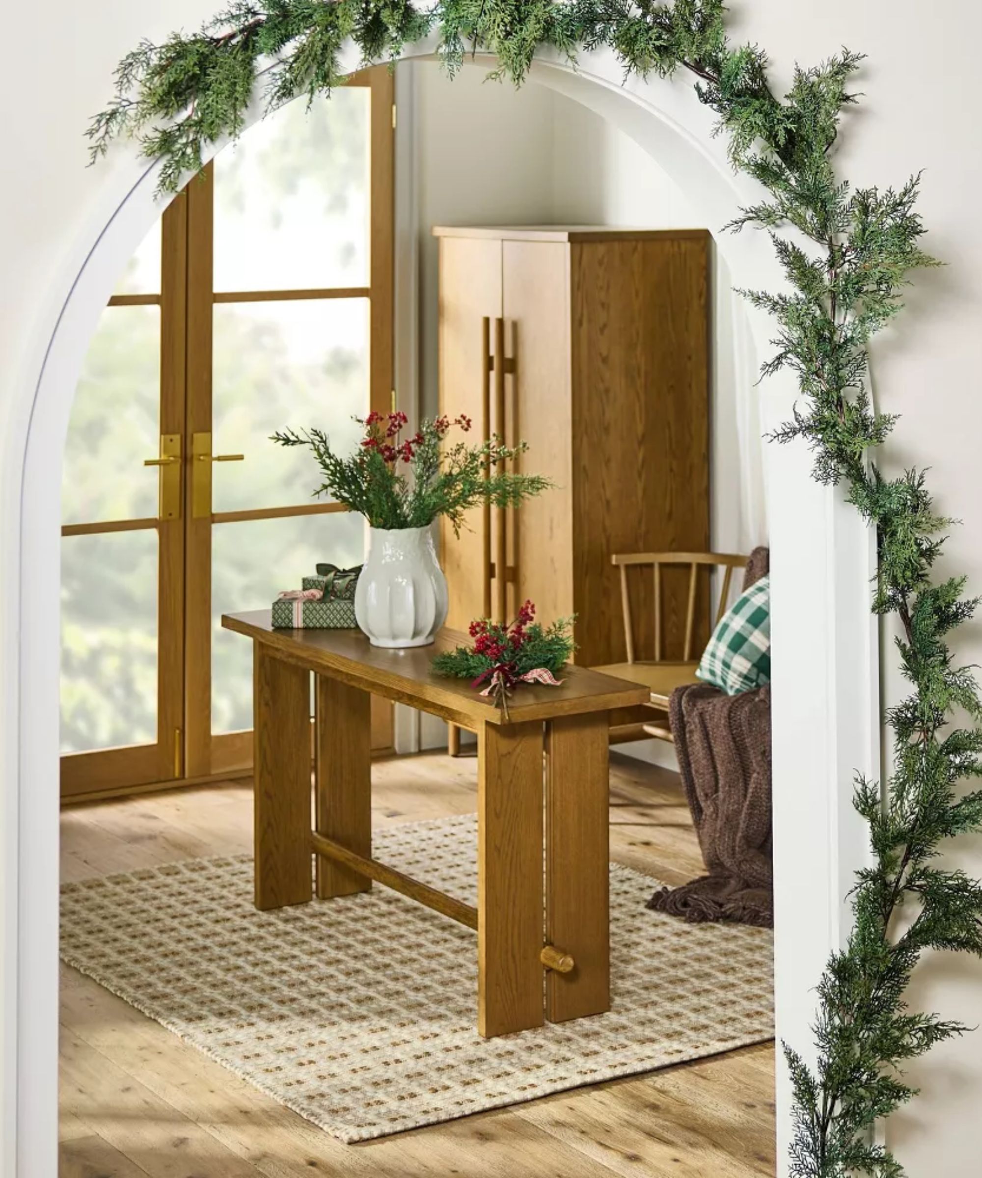 Faux garland over archway leading to wood table covered with faux branches and berries