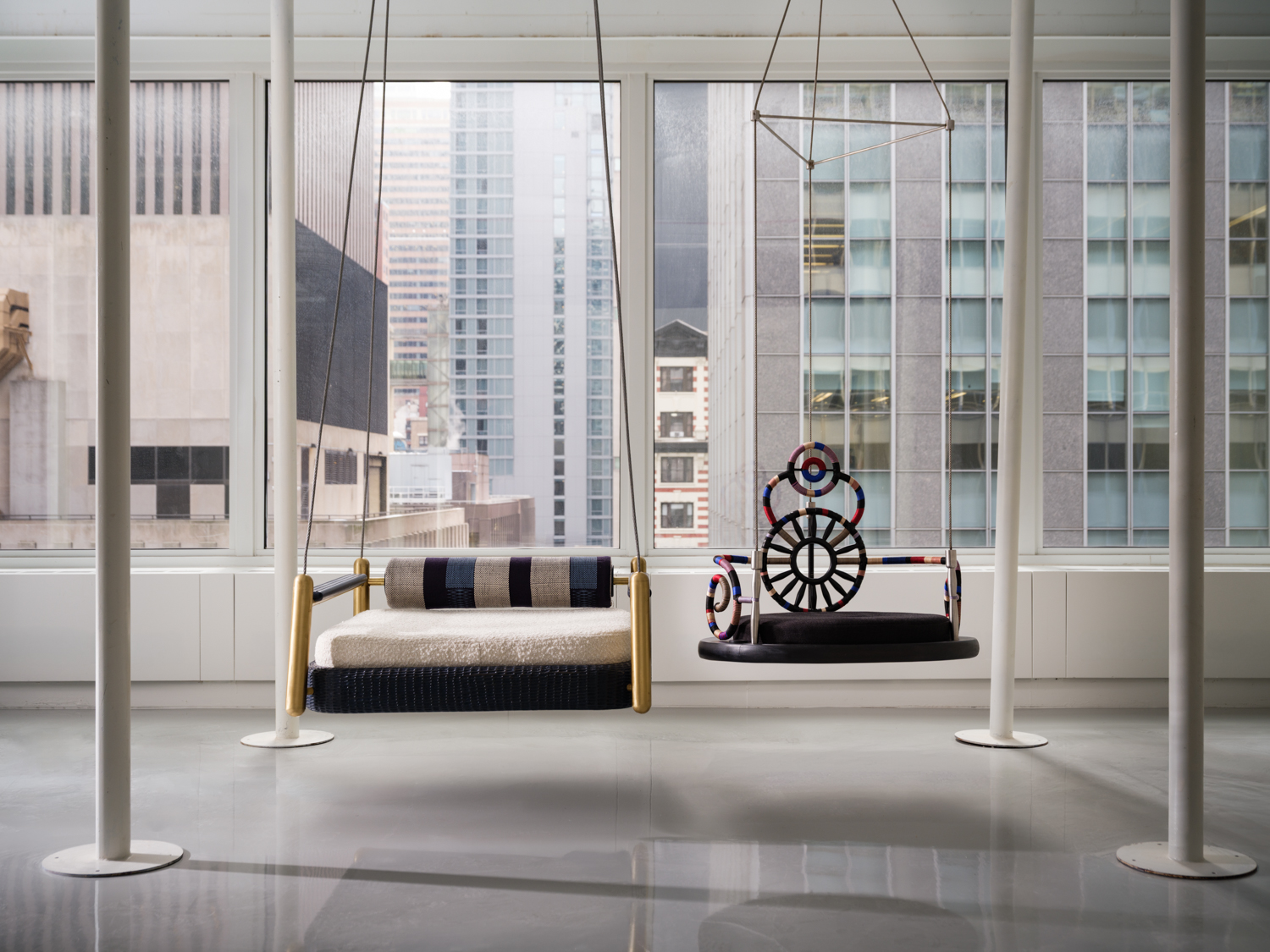 An exhibition in NYC's midtown district at House of Santal, where two suspended chairs hang above a polished concrete floor with business buildings in the background.