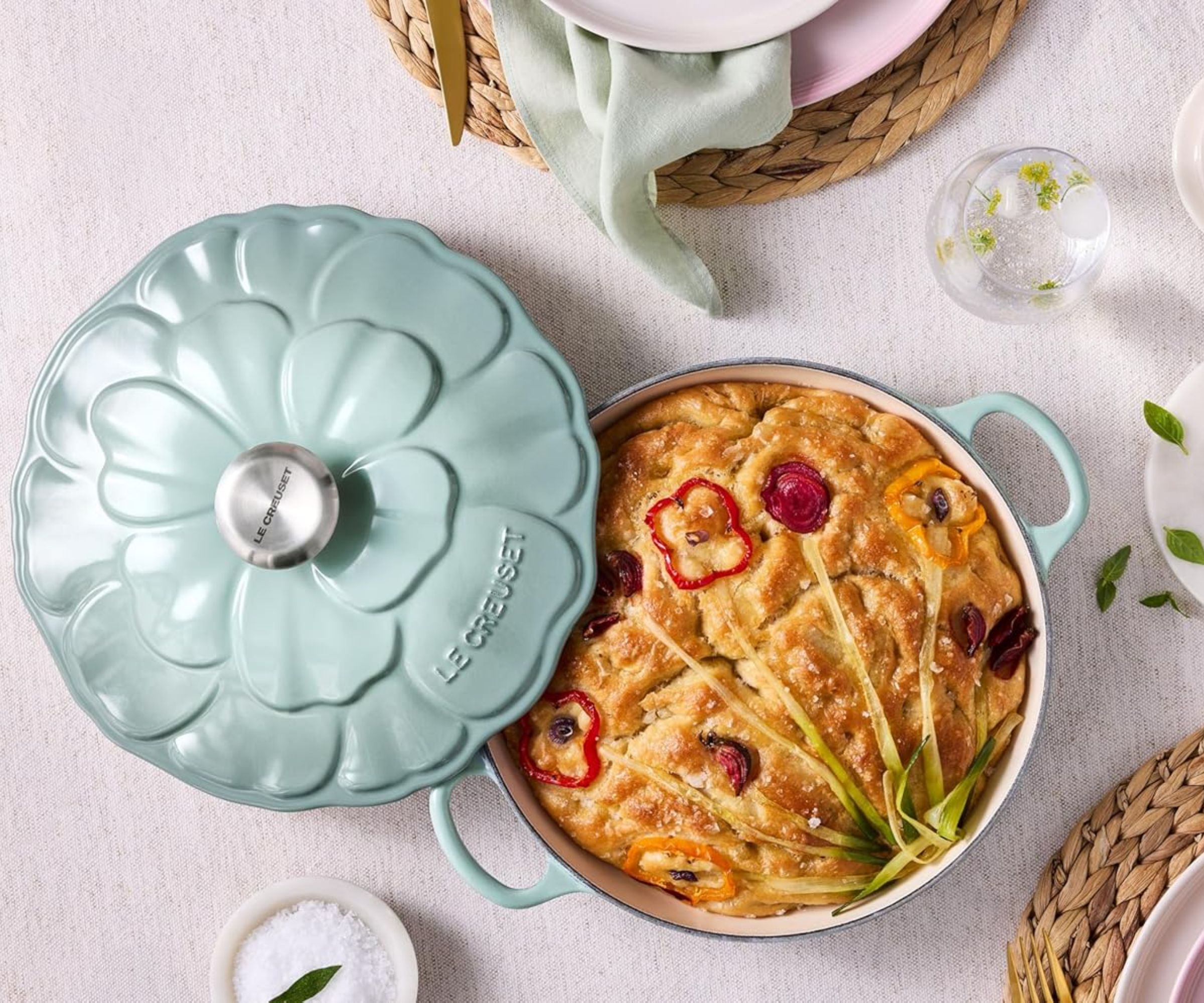 A blue brasier embossed with a petal design, on a pink clothed table. A baked focaccia is inside.