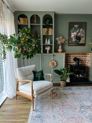 A living room with a boucle armchair and a built in billy bookcase painted sage green