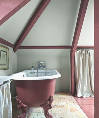 A red and grey bathroom with rolltop bath, beams, tiles and white curtains