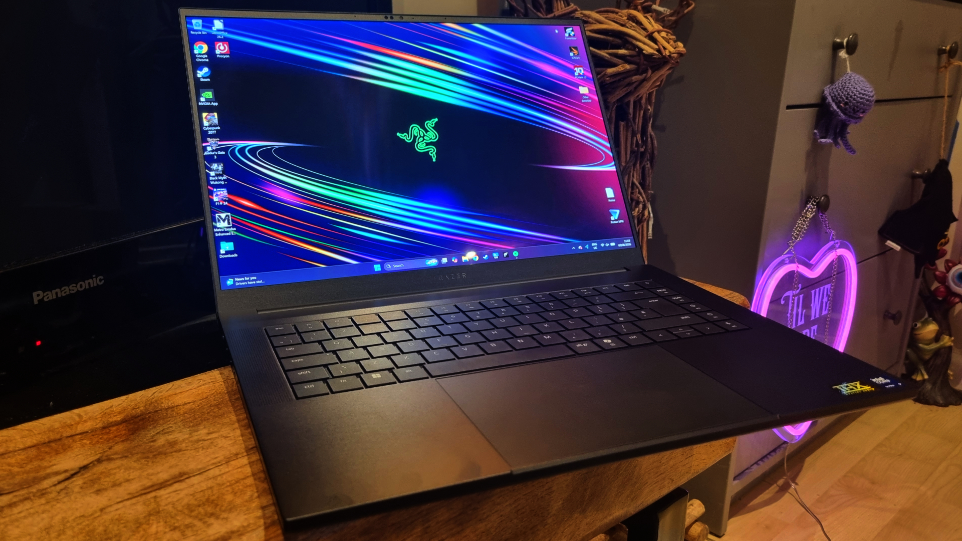 A Razer Blade 16 gaming laptop in front of a TV with a neon sign in the background