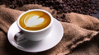 A espresso with late art on the top in a white coffee cup and saucer next to a hessian sack and coffee beans