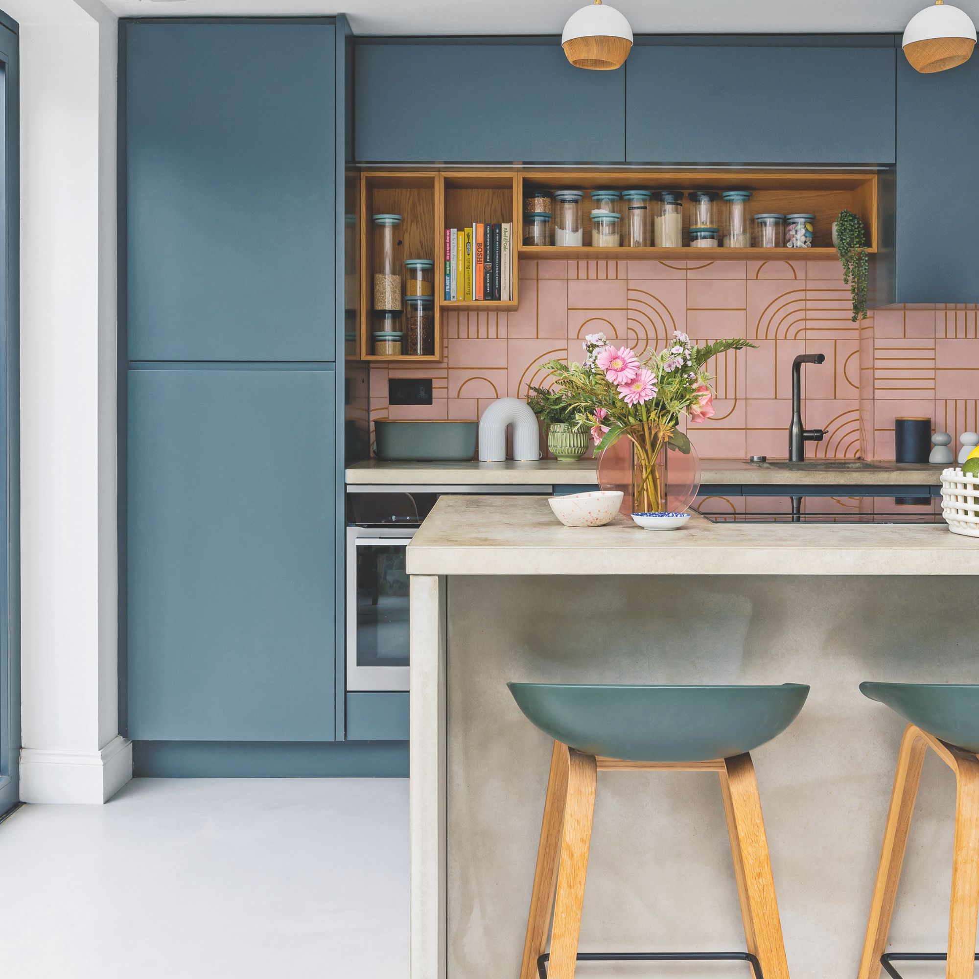 Blue kitchen with a concrete kitchen island and pink tiles behind the sink