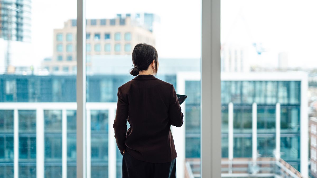 A female CEO standing with her back to the camera, looking out of a high-rise office window, to represent the venture capital gender gap.