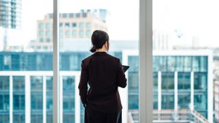 A female CEO standing with her back to the camera, looking out of a high-rise office window, to represent the venture capital gender gap.