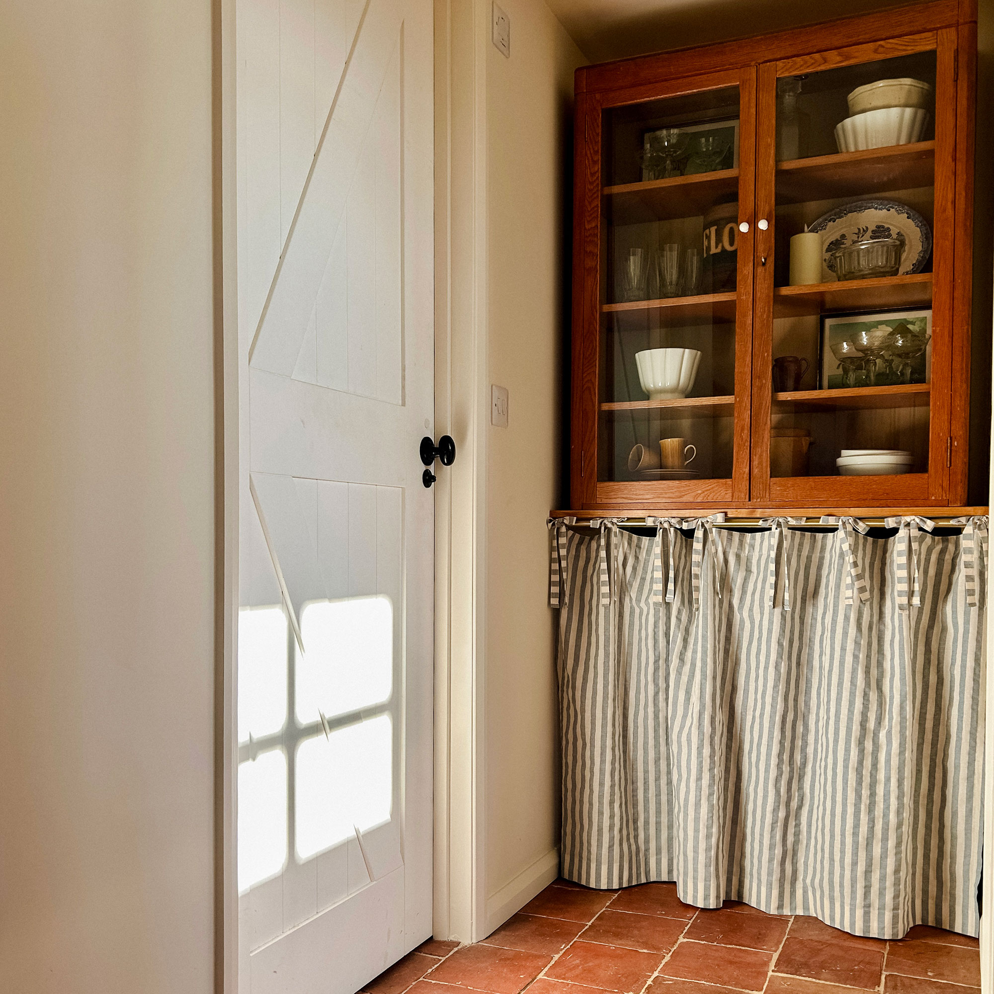 Corner of kitchen with cafe curtain below cupboard