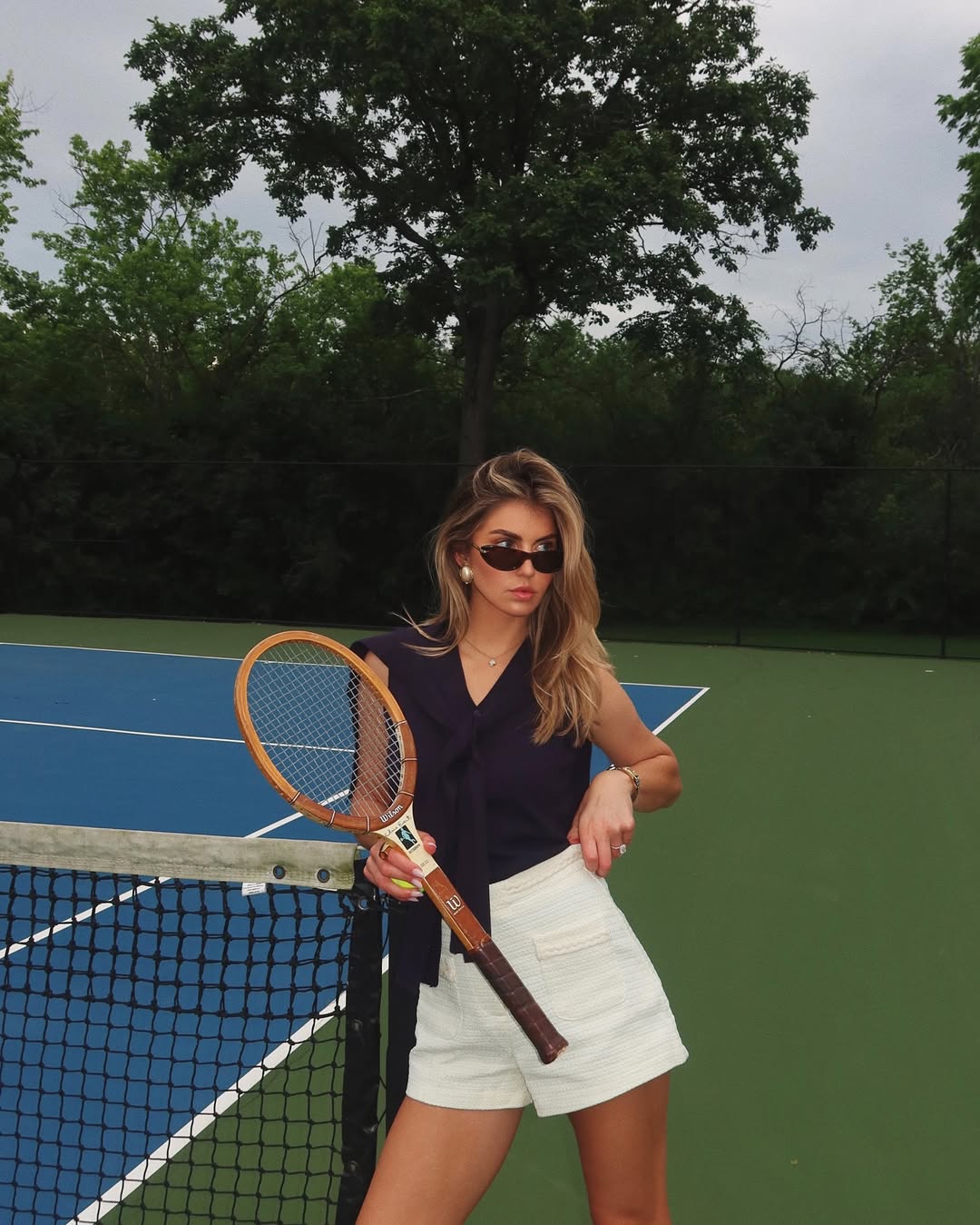 Lexi in a navy tank and white shorts with a tennis racket