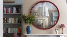 A round mirror above a mantlepiece, beside a bookshelf.