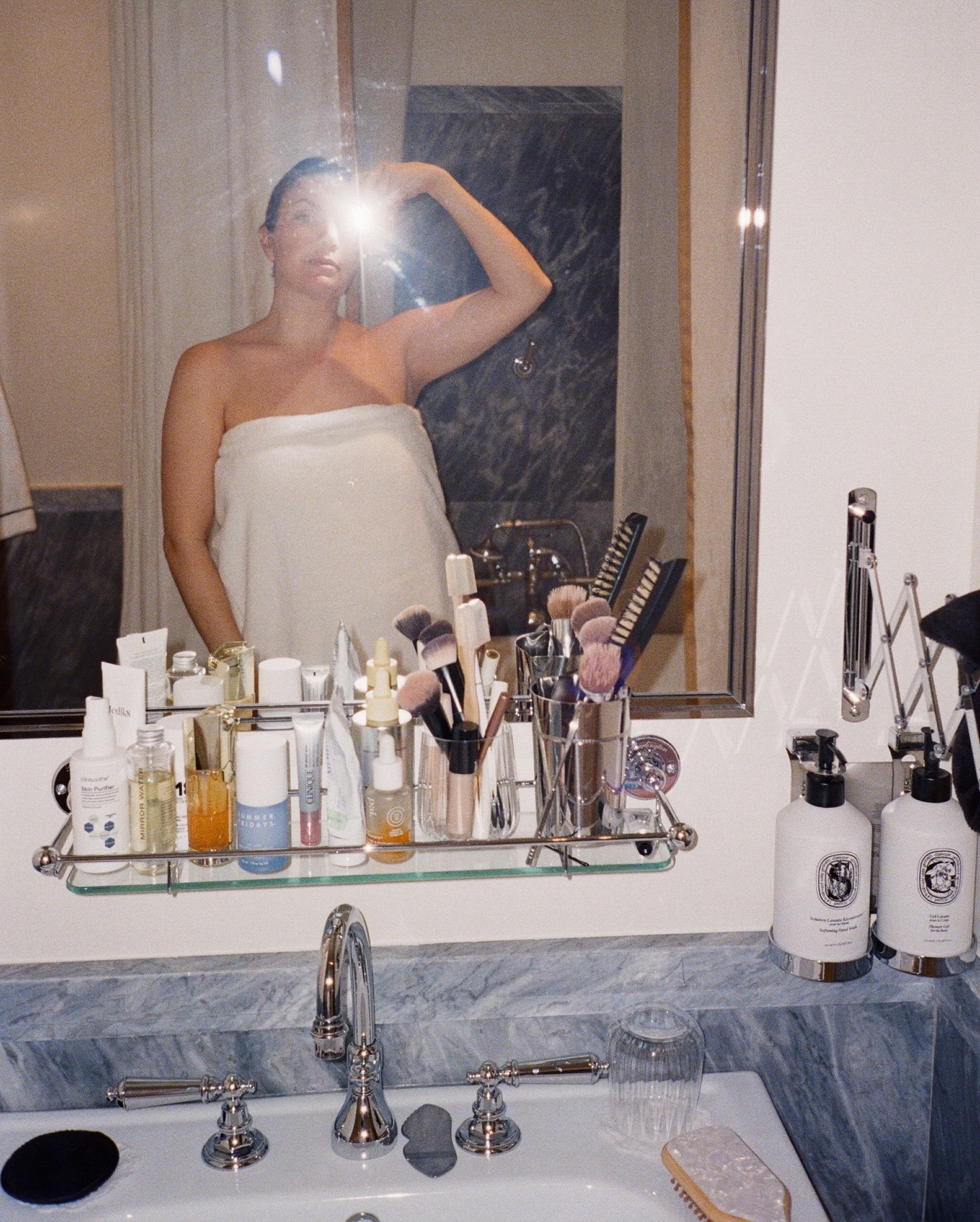 A woman wearing a white towel taking a selfie in the bathroom mirror