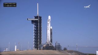 A SpaceX Falcon Heavy rocket on the launch pad at dawn with its reflection in the bay nearby