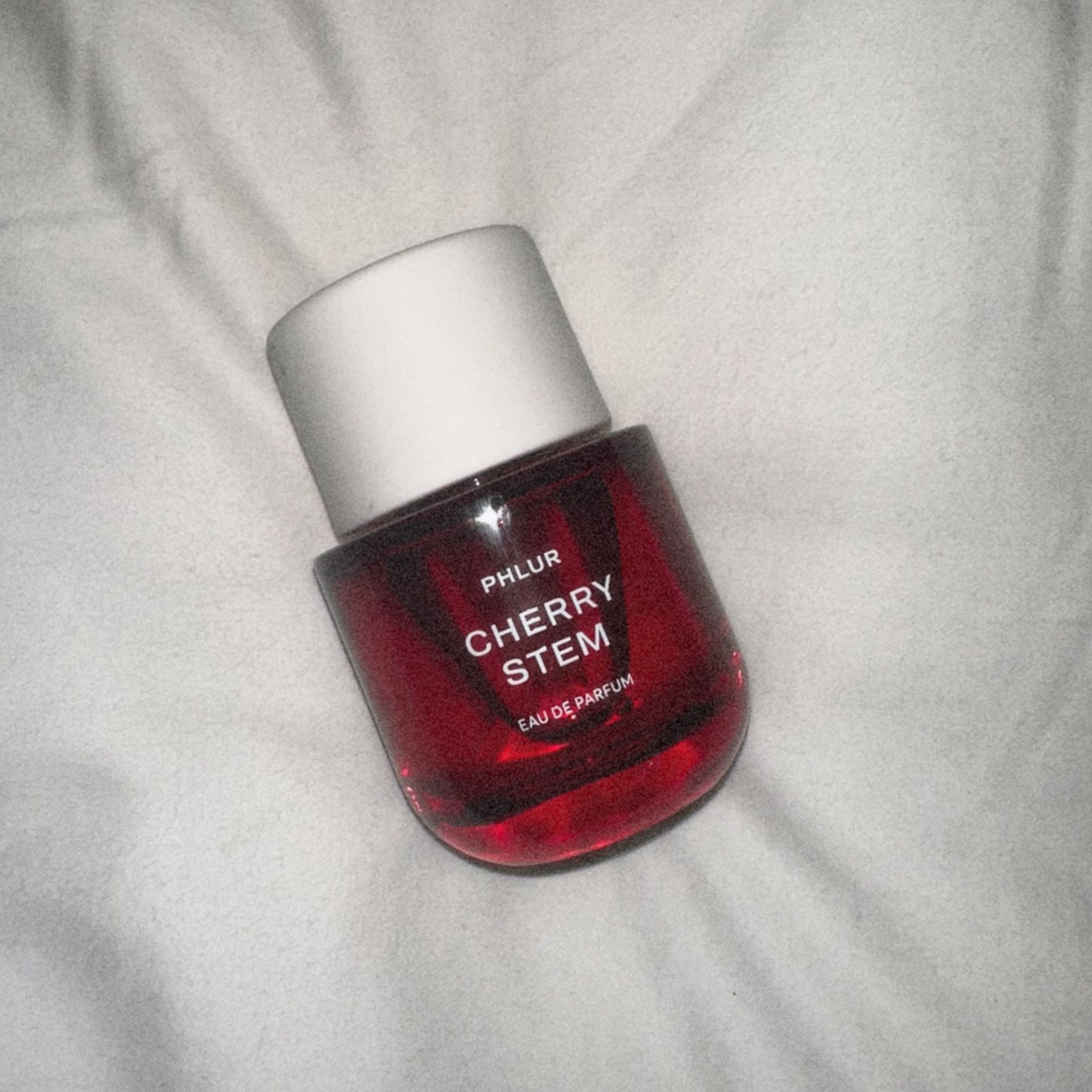 Bottle of Phlur's Cherry Stem Eau de Parfum on a white sheet.