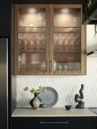 Wooden cabinets with ribbed glass fronts, illuminated by built-in spotlights within the cabinet.