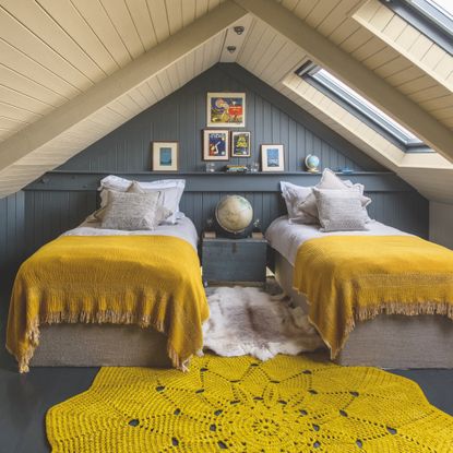 how to make a guest room look expensive, loft bedroom with twin beds, grey tongue and groove walls, stone tongue and groove ceiling, globes, crochet style rug, yellow throws 