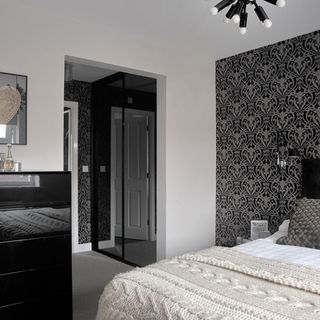 bedroom with bed with cushions black wardrobes damask wallpaper and funky ceiling light