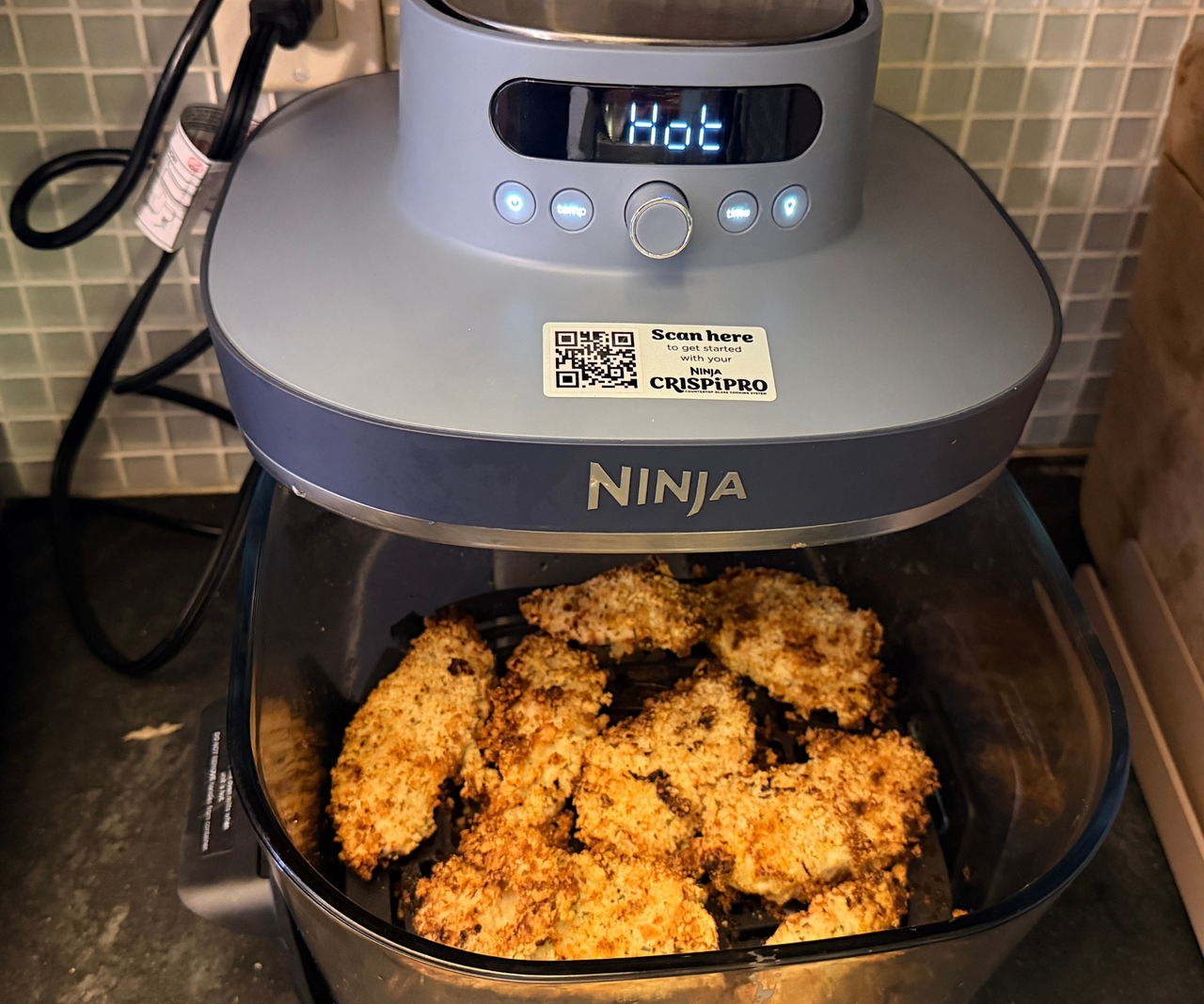 A deep glass air fryer dish filled with breaded chicken, partially pulled out from underneath a blue air fryer head.