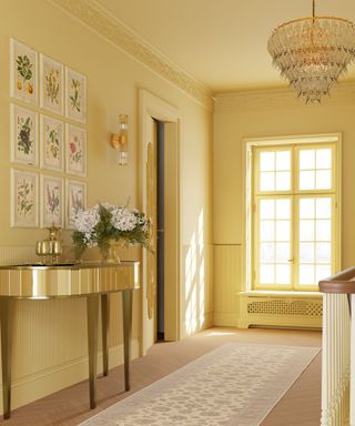 A yellow entryway with a wall with botanical prints, a gold console table, and a wooden floor with a beige floor runner