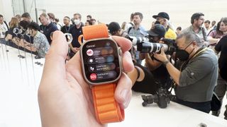 En hand som håller upp en Apple Watch Ultra med ett orange armband.