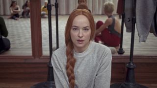 A still from the movie Suspiria showing Susie (played by Dakota Johnson) looking scared at the camera with her red hair in a long plait.