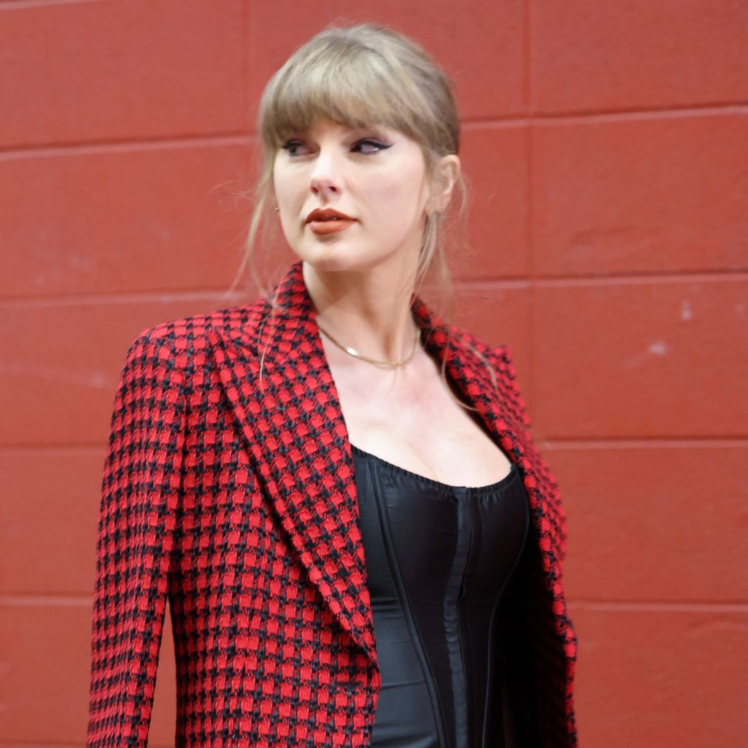 Taylor Swift walks into Arrowhead stadium wearing a red skirt suit by Versace and a gold choker necklace