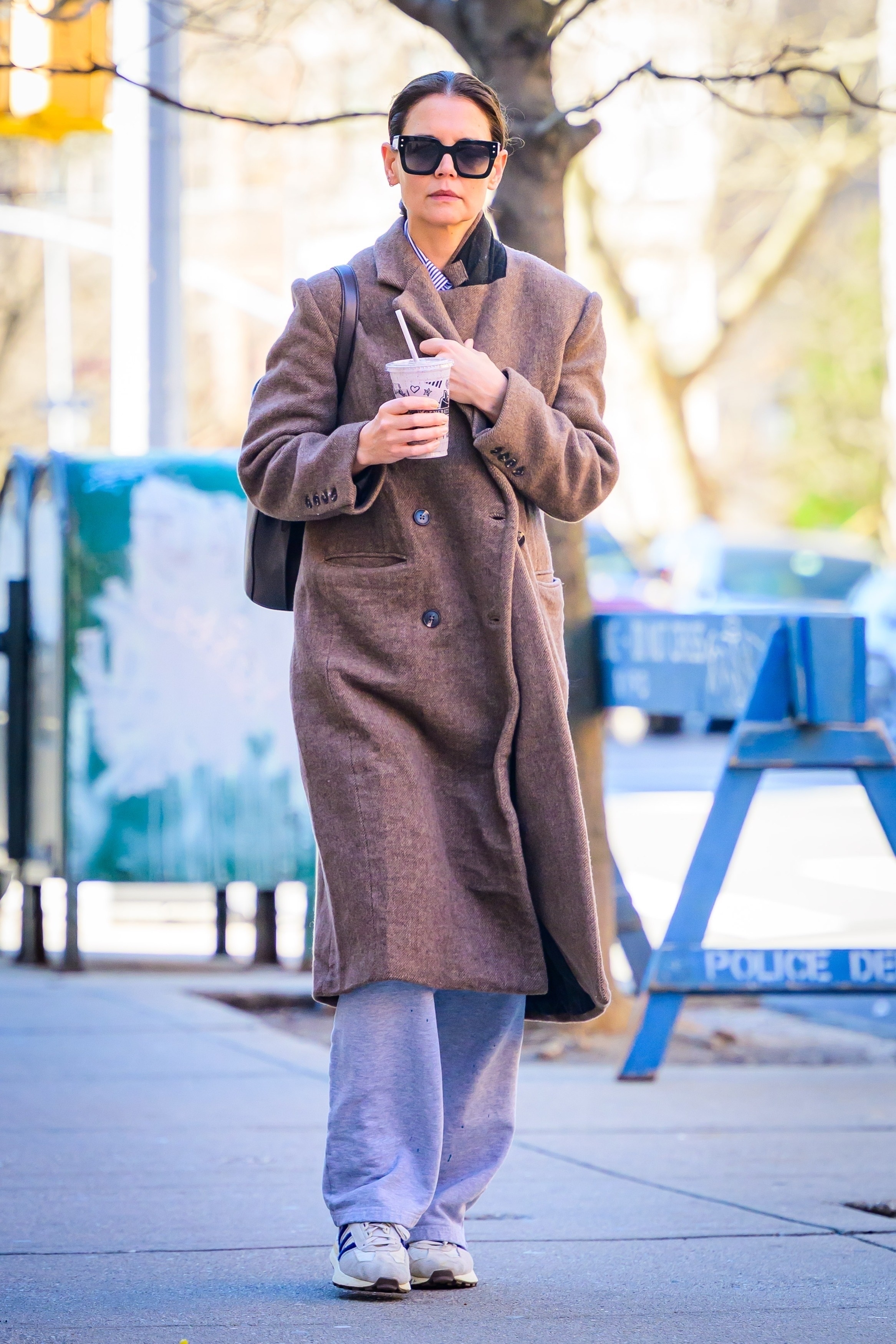 Katie Holmes wears sunglasses, a long coat, gray sweatpants, and adidas sneakers.