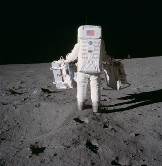 Apollo 11 astronaut Buzz Aldrin holds two experiments that he and Neil Armstong left behind on the moon. In his right hand is a corner cube reflector, the first of five that NASA astronauts eventually deposited on the lunar surface.