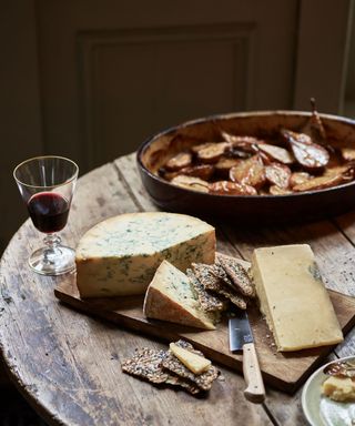 cheese platter on wooden dining table with glass of red wine