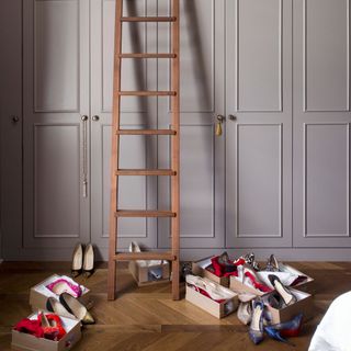 Grey fitted wardrobes, with a wooden ladder leaning against it and boxes of shoes on the floor