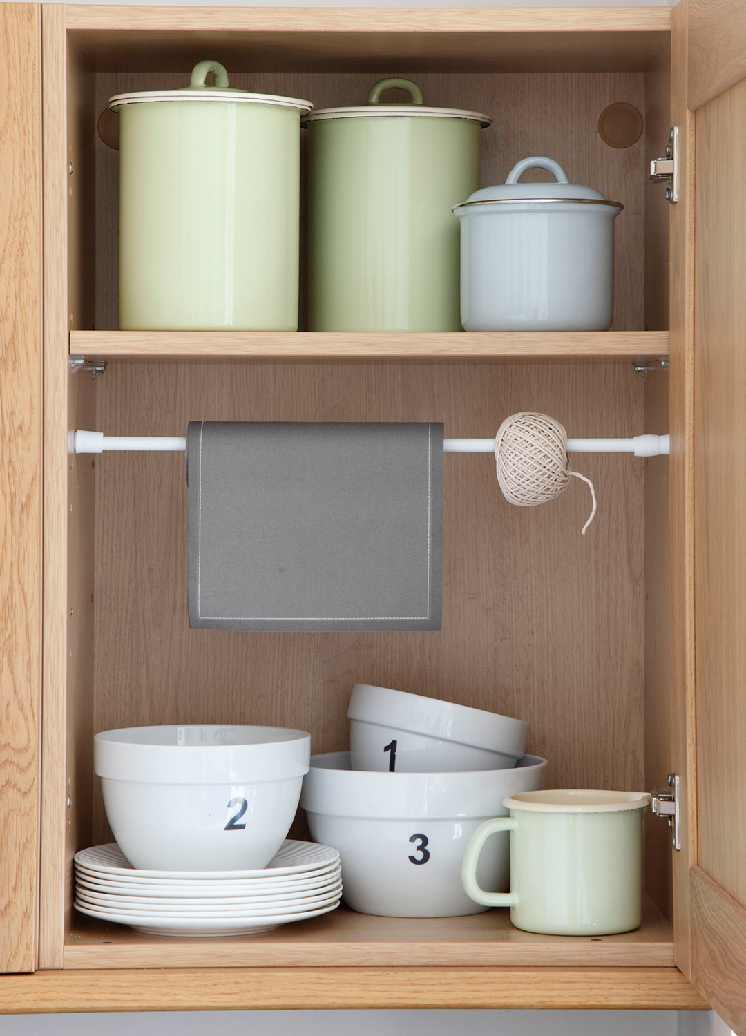 Inside a wooden kitchen cupboards with stacked plates and bowls, a tension pole for storage