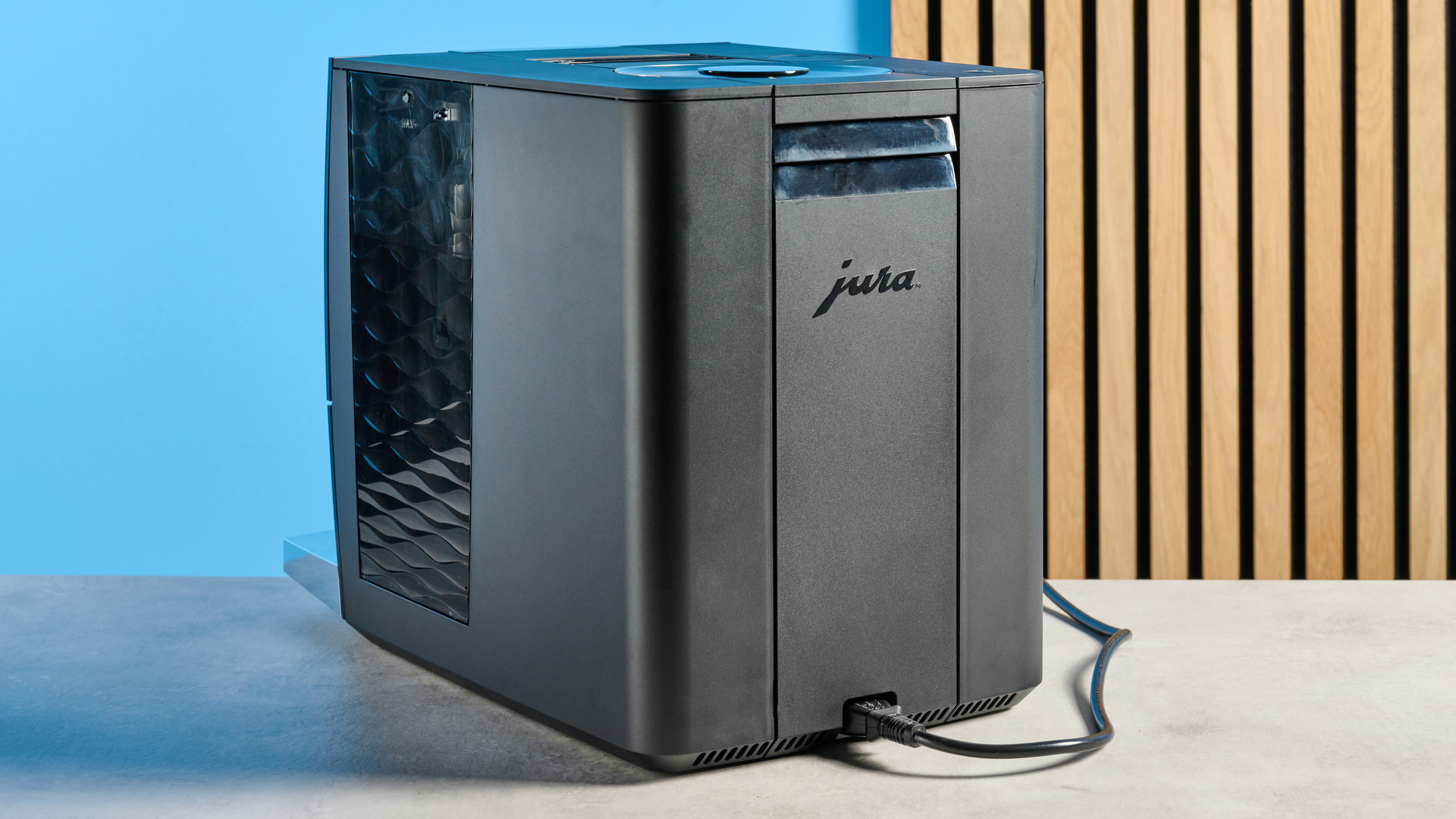 the jura c8 automatic coffee machine in piano black photographed with a blue and wood background
