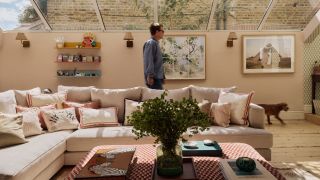 Image of Thomas Straker walking through a light pink living room that has a large skylight and a large, light pink sectional sofa.