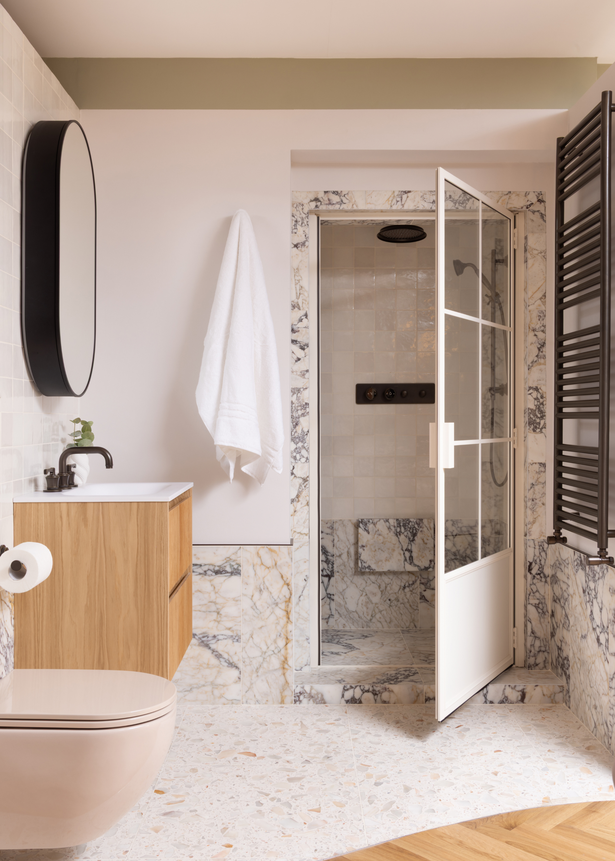 A white bathroom with a terrazzo floor, a marble and tile steam shower room, a mounted radiator, a floating sink cabinet and a mirror