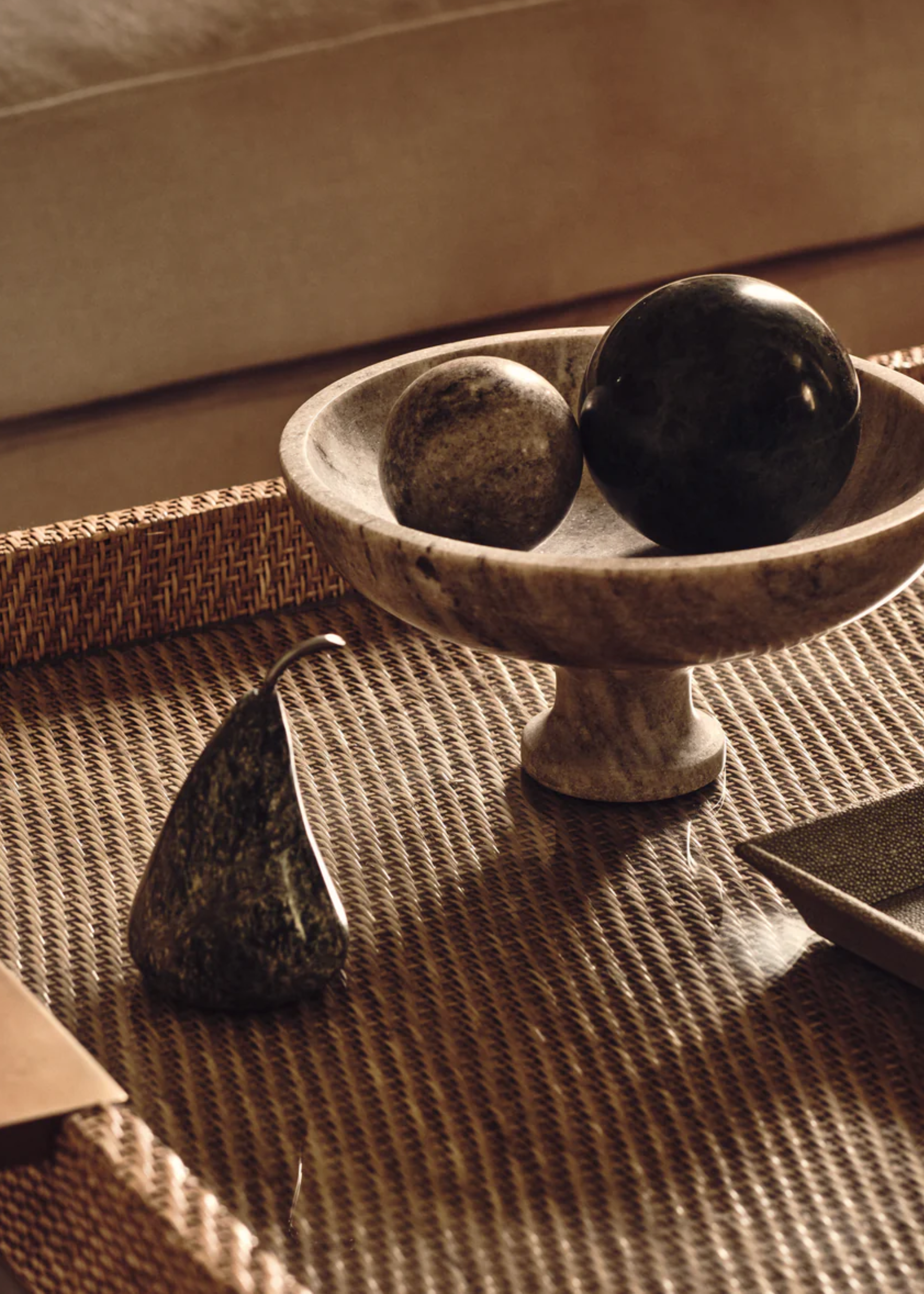 a marble pear decoration next to marble ball decor in a marble bowl on top of a rattan coffee table