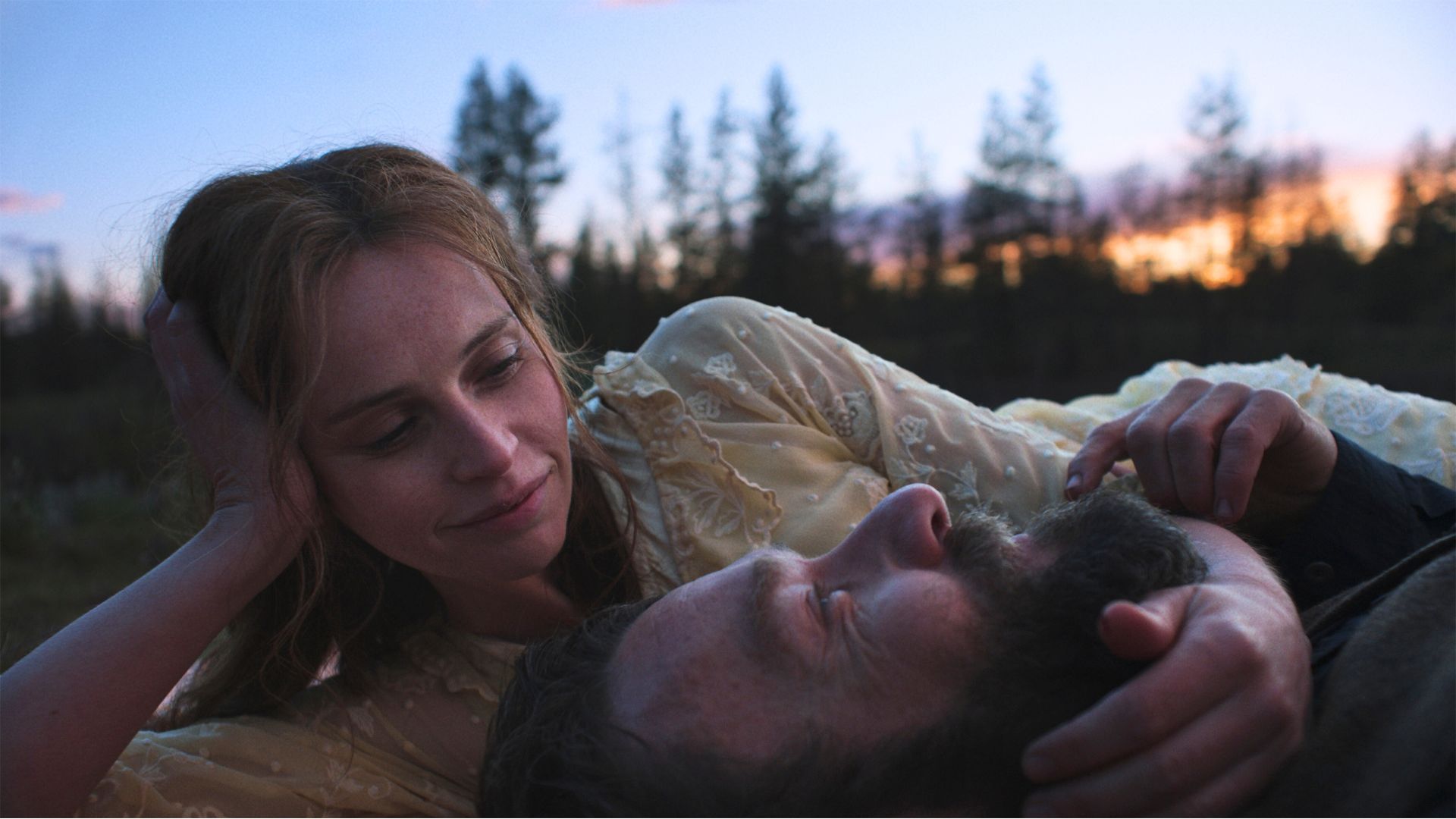 Felicity Jones holds Joel Edgerton&#039;s face as they lie in the grass