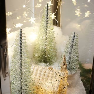 Close up of wire brush Christmas trees surrounded by fairy lights and fake snow