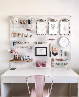 A decorated pegboard next to a desk with a pink chair