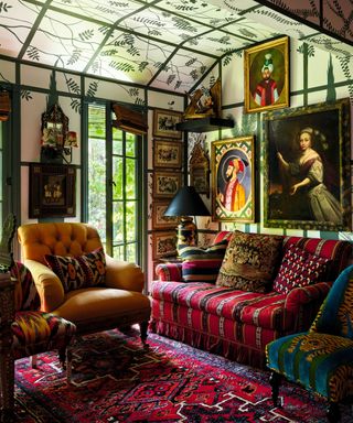 maximalist living space with sofa and armchair and foliage painted on ceiling