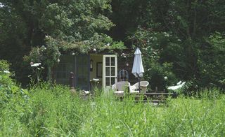 a summerhouse buried within the end of a cottage garden, with outdoor dining set and a parasol